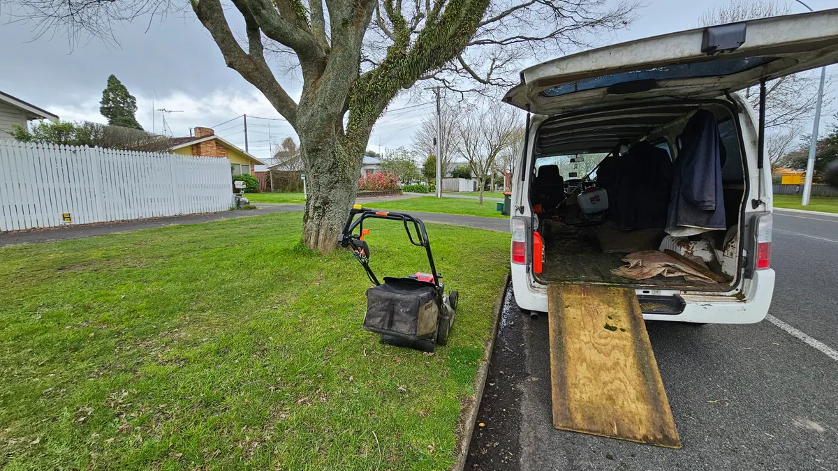 Lawn mowing van with the ramp down and a mower on a customer's lawn