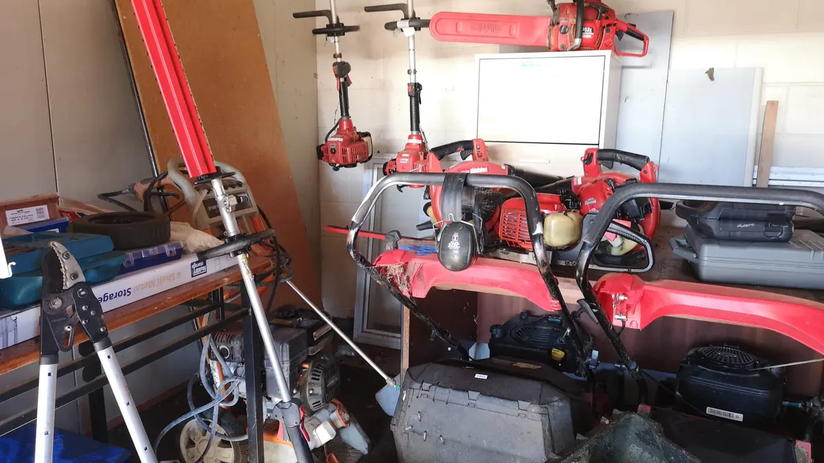 A garage packed with red push mowers, line trimmers, blowers, hedge trimmers and a chainsaw