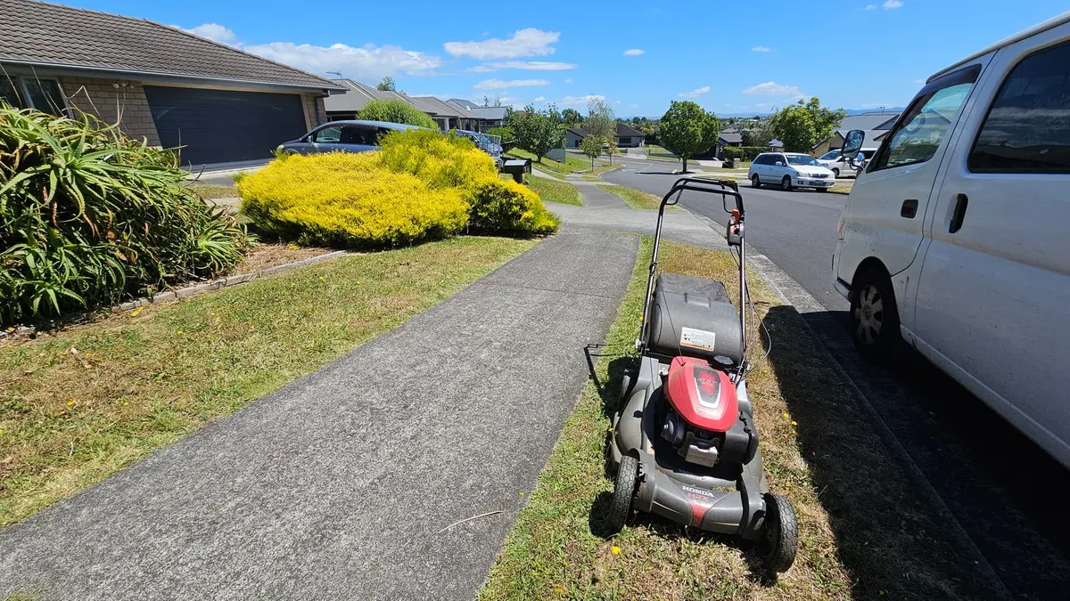 Honda mower on a berm beside the footpath with the white van parked at the kerb